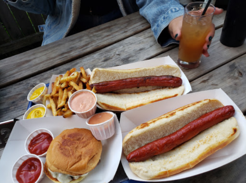 A table with two hot dogs, a burger, fries, and dipping sauces, alongside a drink in a glass.