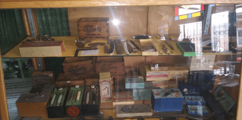 Display case filled with various vintage knives, scissors, and packaging from a cutlery company.