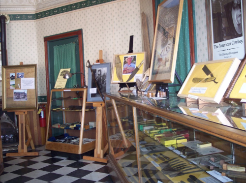 Interior of a museum display featuring framed photos, artifacts, and informational signs on a checkered floor.