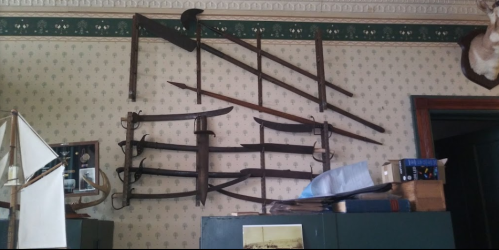 A collection of vintage tools and weapons displayed on a wall, including swords and farming implements.