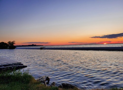 A serene sunset over a calm lake, with vibrant orange and purple hues reflecting on the water's surface.