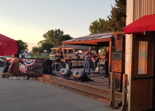 A band performs on an outdoor stage at sunset, with a crowd enjoying the music in the background.