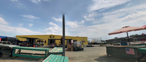 A yellow building with outdoor seating and various equipment, under a partly cloudy sky.