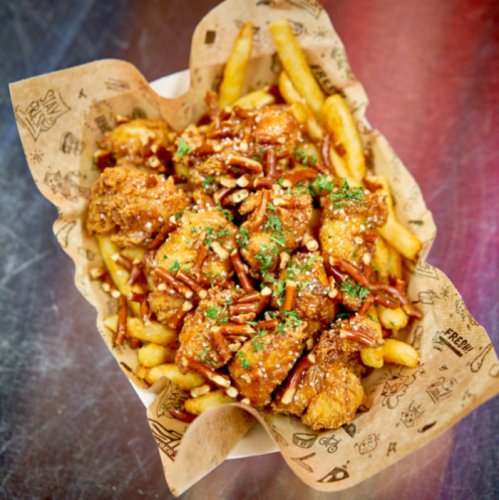 A basket of crispy fried chicken pieces topped with nuts and herbs, served over a bed of golden French fries.