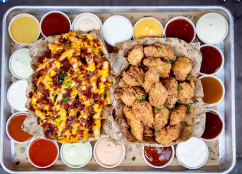 A tray featuring crispy fried chicken and loaded cheese fries, surrounded by various dipping sauces.