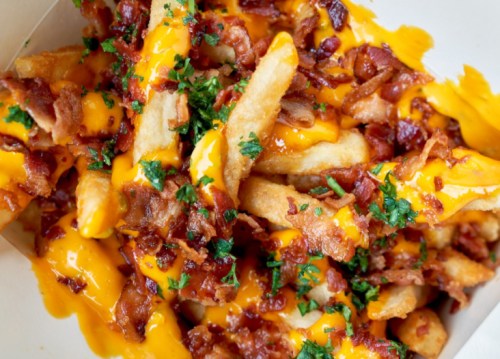 A close-up of loaded fries topped with melted cheese, crispy bacon bits, and fresh parsley.
