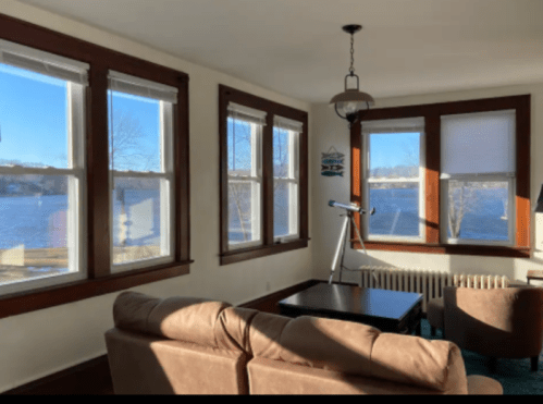 Cozy living room with large windows overlooking a lake, featuring a telescope and comfortable seating.