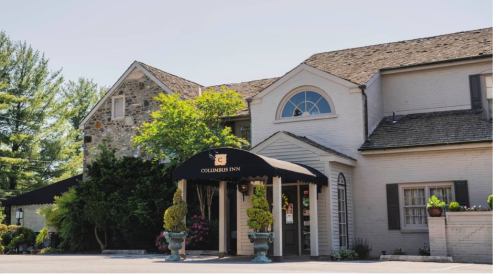 A charming inn with a stone and brick exterior, featuring a black awning and lush greenery around the entrance.