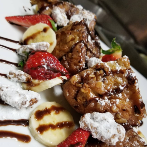 A plate of dessert featuring chocolate-drizzled pastries, strawberries, bananas, and powdered sugar.