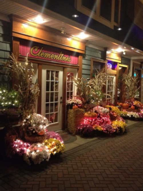 A cozy restaurant entrance adorned with autumn decorations, including pumpkins and colorful flowers, illuminated at night.