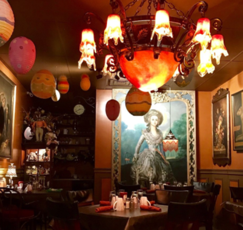 Cozy restaurant interior with a chandelier, colorful hanging decorations, and vintage artwork on the walls.
