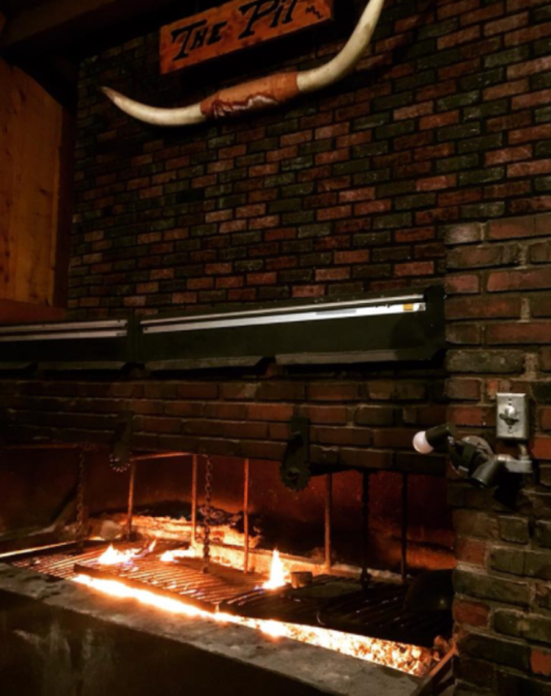 A rustic brick grill with flames, featuring a large bullhorn mounted on the wall above.
