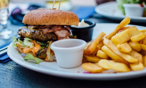 A hearty burger with bacon, lettuce, and tomato, served with a side of golden fries and dipping sauce.