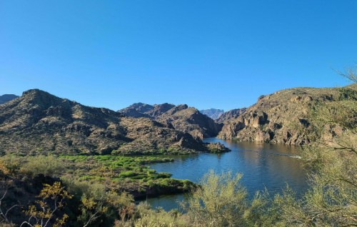 A serene landscape featuring a river winding through rocky hills and green vegetation under a clear blue sky.