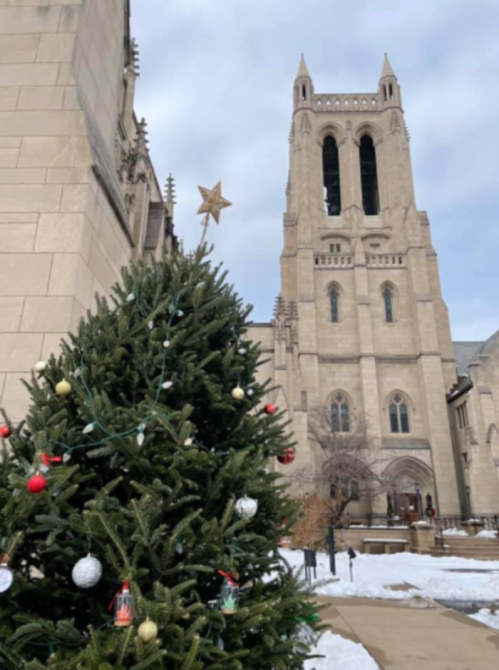 A decorated Christmas tree in front of a tall stone church tower on a snowy day.