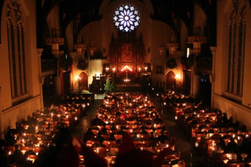 A dimly lit church filled with people holding candles, illuminated by a large stained glass window.