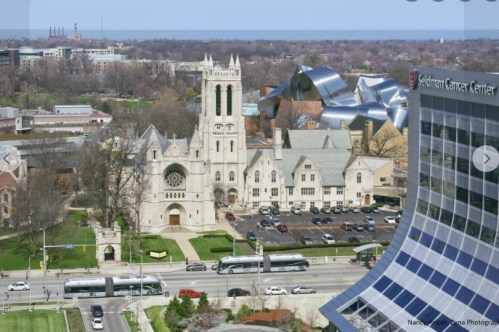 Aerial view of a cityscape featuring a historic church, modern buildings, and a glimpse of the lake in the background.