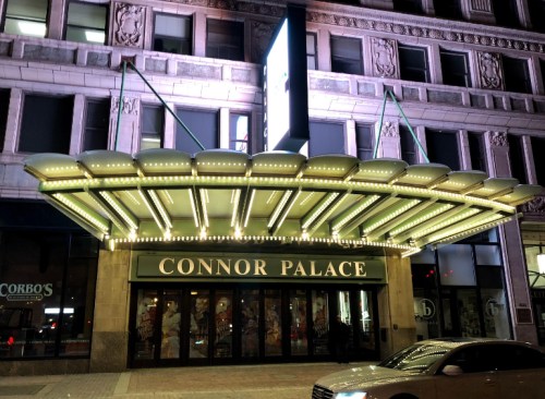 The illuminated entrance of the Connor Palace theater, featuring a marquee and decorative lights at night.