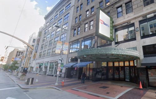 A street view of a building with a U.S. Bank sign, featuring a glass entrance and nearby storefronts.