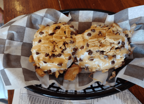 Two dessert bowls topped with crushed cookies, chocolate chips, and drizzled caramel, served in a checkered paper-lined basket.