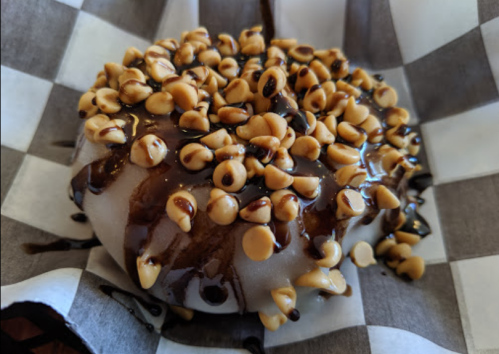 A close-up of a donut topped with chocolate drizzle and sprinkled with mini chocolate chips on a checkered paper.