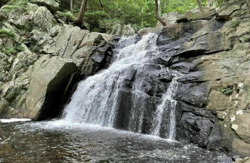 A serene waterfall cascading over rocky terrain, surrounded by lush green trees and a calm pool below.