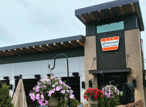 Exterior of Lakewood Truck Park with hanging flower baskets and a modern design, under a cloudy sky.