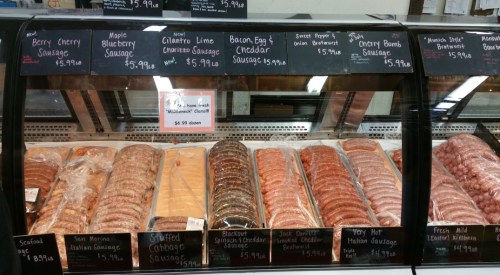 Display case filled with various types of sausages, each labeled with prices and names.
