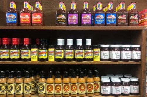 A wooden shelf displaying various bottles of sauces and condiments in colorful packaging.