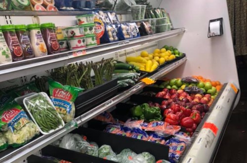 A grocery store display featuring fresh vegetables and fruits, including asparagus, peppers, apples, and greens.