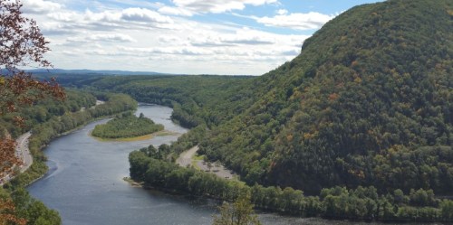 A scenic view of a winding river surrounded by lush green hills under a partly cloudy sky.