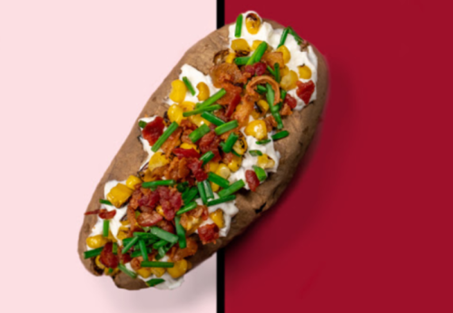 Baked potato topped with sour cream, corn, bacon, and chives on a split pink and red background.