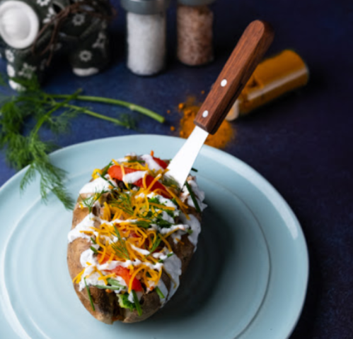 Baked potato topped with cheese, vegetables, and sour cream, served on a light blue plate with seasonings in the background.
