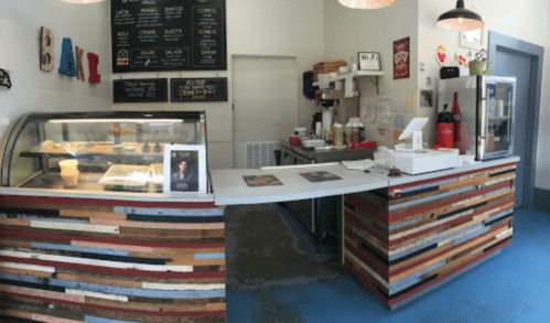 A cozy café counter with a display case, colorful wooden accents, and a menu board on the wall.