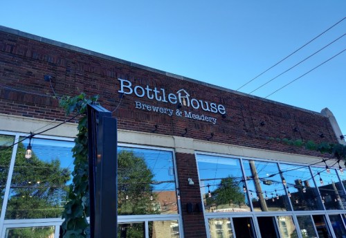 Exterior of Bottlehouse Brewery & Meadery, featuring a brick facade and large windows under a clear blue sky.