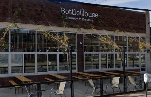 Exterior of BottleHouse Brewery & Meadery, featuring large windows and outdoor seating with wooden tables.