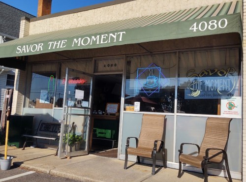 Exterior of "Savor the Moment" café, featuring a green awning, open door, and two chairs outside.