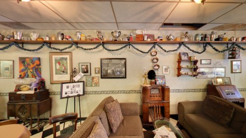 Cozy café interior with a decorated wall featuring vintage items, artwork, and a shelf of memorabilia above a seating area.