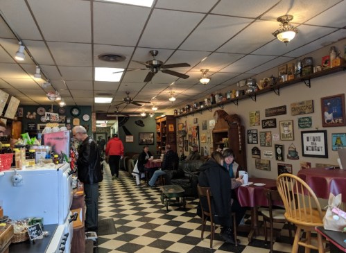 A cozy café interior with checkered floors, tables, and vintage decor, featuring patrons enjoying their meals.