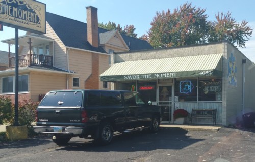 A black truck parked outside a small café with a green awning, surrounded by trees and a residential building.