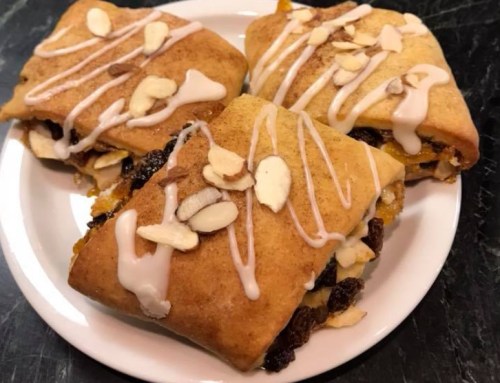 Three pastry squares topped with sliced almonds and drizzled with icing, served on a white plate.
