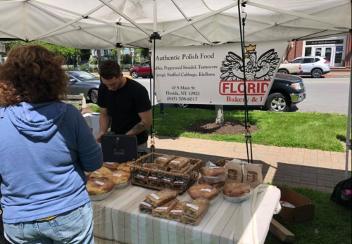 A vendor at a market stand selling Polish baked goods under a tent, with a sign for "Florida Bakery & Deli."