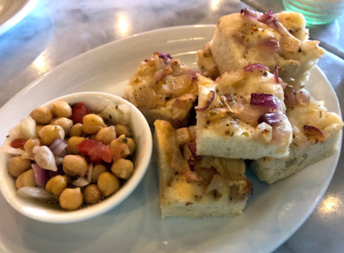 A plate of four pieces of focaccia topped with onions, alongside a small bowl of chickpea salad.