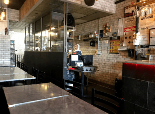 A cozy restaurant interior with marble tables, a counter, and a staff member in a hijab behind the service area.