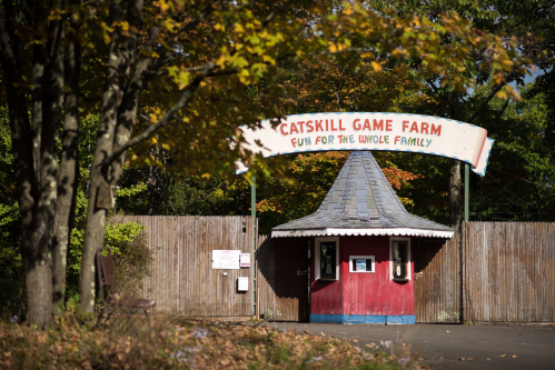 Entrance to Catskill Game Farm, featuring a colorful sign and rustic wooden fence, surrounded by autumn foliage.