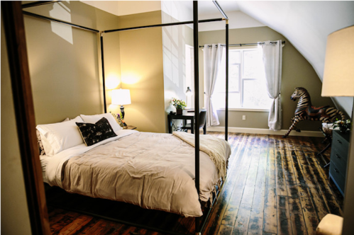 Cozy bedroom with a four-poster bed, wooden floors, and a decorative zebra statue in the corner. Natural light from the window.
