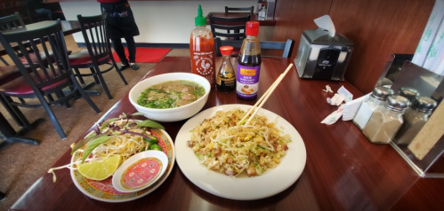 A table with a plate of fried rice, a bowl of soup, and condiments including sriracha and soy sauce.