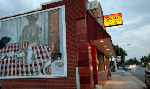 Exterior of Sully's Steak House & Bar, featuring a mural of a woman in a red-checkered dress on the side wall.
