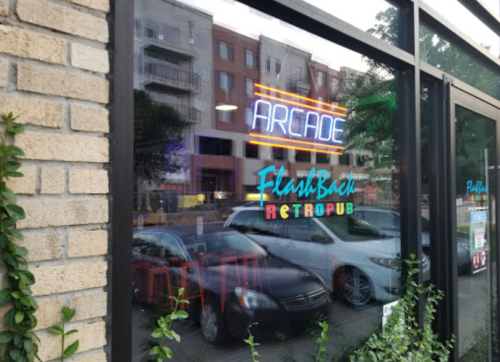 A storefront window displaying neon signs for "Arcade" and "FlashBack Retropub" with cars parked outside.