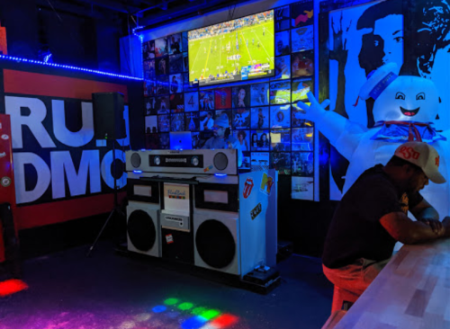 A vibrant bar scene featuring a large boombox, a TV showing a game, and a Stay Puft Marshmallow Man decoration.